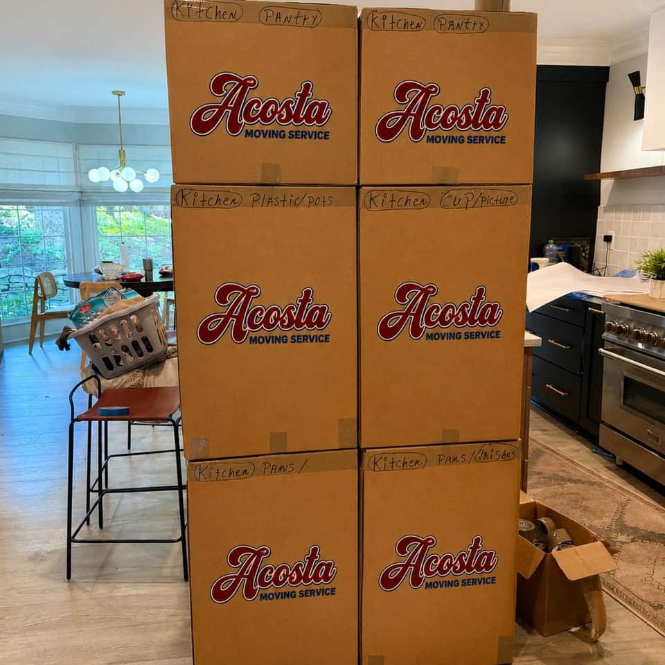 Labeled Acosta Moving Service kitchen boxes stacked in a living room, ready for loading